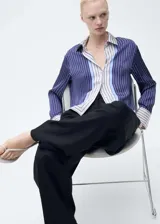 Camisa de manga larga con estampado de rayas verticales azules y blancas, confeccionada en tejido fluido con acabado satinado. Presenta cuello camisero, cierre frontal con botones y puños abotonados. Diseño recto y calce regular.