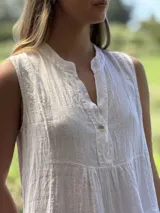 Vestido verde militar de lino, corte a la rodilla, sin mangas, con cuello mao y botones de nácar. Presenta varios cortes en su largo, aportando movimiento y un toque moderno a este diseño fresco y elegante.