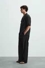 Pantalón negro de corte recto y calce relajado, confeccionado en tejido de algodón con elasticidad. Presenta cintura ajustable con cordón, bolsillos frontales y bolsillos traseros de doble vivo.