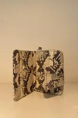 Billetera pequeña con estampado de piel de cocodrilo en tonos beige y marrón. Cierre con broche a presión y correa de muñeca.