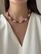 Gargantilla corta con cuentas de colores rojo, azul, blanco y beige con manchas negras. Se cierra con cadena de acero quirúrgico y ganchito para regular el largo.