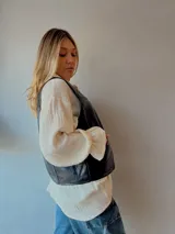 Chaleco negro de cuero con botones metálicos y bolsillos delanteros.