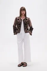 Chaqueta corta de algodón color marrón topo, sin cuello, con bordados florales y de estilo paisley en negro. Presenta un borde festoneado y mangas largas.