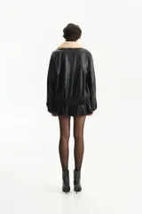 Chaqueta estilo aviador de cuero sintético negro, con cuello de pelo sintético color crema. Presenta cierre frontal y bolsillos con solapa en el pecho.
