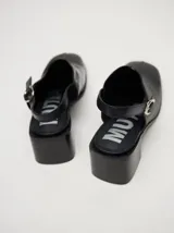Mocasines color beige con taco bloque de madera color negro y correa trasera ajustable.