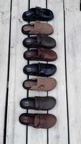 Zuecos cerrados de cuero marrón oscuro, con puntera redonda y tira ancha con hebilla metálica y ojales.