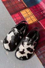 Zuecos con estampado de vaca en blanco y negro, con tira de cuero sintético negra con hebilla.