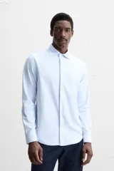 Camisa celeste a rayas verticales blancas, de corte recto, con cuello italiano abierto, manga larga con puños abotonados y cierre frontal con botones.