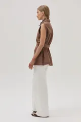 Chaleco largo marrón de algodón con cuello camisero, cierre frontal con botones, bolsillos laterales y lazo ajustable en la cintura.