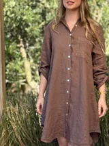 Vestido camisero blanco de lino, con cuello camisero, manga larga con botón para recoger, cierre frontal con botones de nácar, bolsillo en el pecho y diseño asimétrico más largo en la parte trasera.