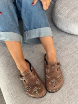 Zuecos marrones de cuero con hebilla metálica y detalles de bordado artesanal, tachas y remaches.