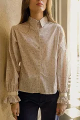 Camisa de algodón con estampado floral, cuello clásico, cierre frontal con botones, mangas largas con puños fruncidos y detalle de puntilla en puños y espalda.