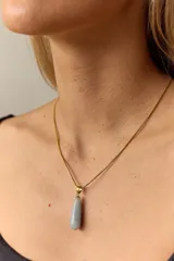 Collar dorado con cadena fina y dije colgante en forma de lágrima de piedra natural azul con vetas blancas.
