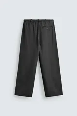 Pantalón negro de corte relajado y pierna ancha, confeccionado en mezcla de algodón y lino. Presenta cintura elástica ajustable con cordón y cierre frontal con cremallera y botón.
