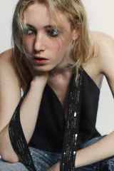 Top negro de tejido satinado con cuello halter que cae en un escote pronunciado y fluido. Presenta tiras largas que caen al frente, adornadas con abalorios brillantes.