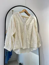 Camisa blanca de manga larga con puños elásticos, cierre frontal con botones y apliques bordados de flores en la parte delantera y trasera.