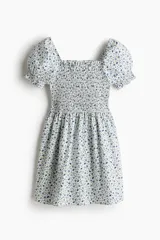 Vestido corto de popelina de algodón con estampado floral azul. Presenta escote cuadrado con elástico, mangas cortas abullonadas con fruncido elástico, cuerpo ajustado fruncido y falda con vuelo.