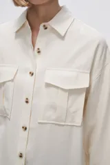 Camisa color crudo de viscosa, corte holgado, con cuello camisero, cierre frontal con botones, manga larga y dos bolsillos con solapa en el pecho.