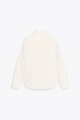 Camisa color crema de corte recto, confeccionada en algodón. Tiene cuello solapa, manga larga con puños abotonados, bolsillo de parche en el pecho y cierre frontal con botones.