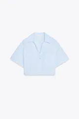 Camisa celeste de popelín con cuello solapa, escote pico y manga corta. Presenta dos bolsillos delanteros de parche y cierre frontal con botones.