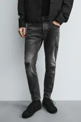 Pantalón de jean negro ajustado al cuerpo desde la cintura hasta el tobillo, de tiro medio y tejido elástico. Diseño de cinco bolsillos con lavado efecto roto y cierre frontal con cremallera y botón.