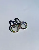 Par de aros colgantes con argollas doradas y dijes circulares de resina transparente con incrustaciones de strass de colores. El dije mide aproximadamente 1.5cm de diámetro.