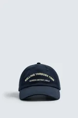 Gorra azul marino con visera y bordado frontal con la frase "Going Through Time Garden District, NOLA" en color crema. Ajuste trasero con hebilla metálica.