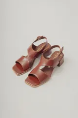 Sandalia de cuero con acabado brillante color marrón rojizo, taco ancho de altura media y punta cuadrada. Presenta tiras anchas cruzadas en el empeine y tira fina con hebilla ajustable en el tobillo.