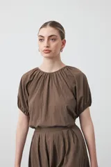 Top negro de manga corta con escote redondo y frunces en la costura de la sisa, creando un efecto de manga abullonada. El tejido parece ligero y con textura.