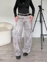 Pantalón jean gris con estampado abstracto, tiro bajo, corte wide leg y cinturón negro.