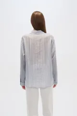 Camisa blanca traslúcida de lyocell, corte holgado, con cuello camisero, cierre frontal con botones y mangas largas con puños abotonados.