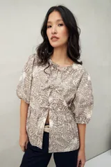 Blusa estampada color beige y blanco, con mangas abullonadas, escote redondo y lazos frontales.