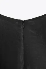 Vestido midi negro de cuello redondo y sin mangas. Corte amplio y fluido, con bolsillos laterales ocultos y cierre trasero con cremallera invisible.