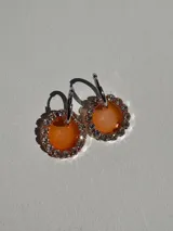 Par de aros colgantes con argolla de acero quirúrgico y dije circular de resina color naranja con borde de strass.