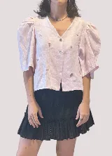 Blusa color rosa pálido de lino con bordados de motivos marinos, escote en V, mangas cortas abullonadas y cierre frontal con botones.