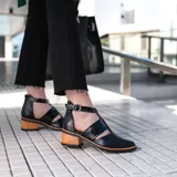 Zapato de cuero negro con detalle de charol, taco de madera con folia en cuero de 5cm, cierre YKK en talón, hebilla y elástico en el empeine.