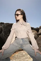 Blusa color beige con cuello mao, mangas largas abullonadas con puños elásticos y volantes en hombros y espalda.