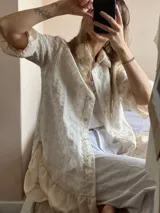 Camisa color crema con bordado floral, de manga tres cuartos con volados irregulares en mangas y ruedo, y largo ligeramente mayor en la espalda.