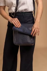 Bandolera de hombro color gris claro, con solapa frontal y correa ajustable. Presenta un diseño simple y práctico, ideal para uso diario.