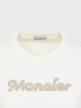 Camiseta blanca de algodón con cuello redondo y mangas cortas. Presenta el logo de la marca Moncler bordado con perlas en el centro del pecho.