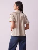 Blusa color beige de gasa estampada, marca Alex & Lili. Tiene cuello fruncido, escote en V con lazo y mangas cortas con volados.