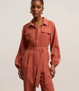 Mono largo color ladrillo, de corte sastrero, con cuello camisero, cierre frontal con botones y cinturón de lazo en la cintura.