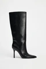 Bota negra de caña alta, confeccionada en cuero sintético, con terminación en punta y tacón fino.