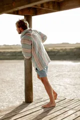 Buzo con capucha de tejido grueso a rayas horizontales en tonos pastel: celeste, rosa y gris. Tiene bolsillo tipo canguro y cordones ajustables en el cuello.