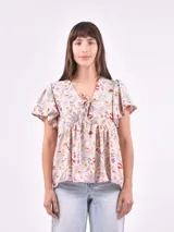 Blusa estampada con cuello en V, mangas cortas con volados y detalle de lazo en el escote.
