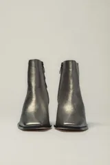 Botín de cuero metalizado color peltre con punta fina y cierre lateral. Tiene taco geométrico de madera color negro.