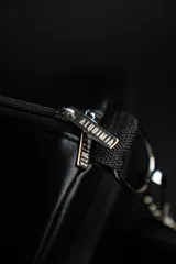 Bolso duffel negro de cuero sintético con logo de ancla bordado en rosa. Tiene doble asa de mano reforzada, correa de hombro regulable y desmontable, cierre superior con doble cremallera y tres bolsillos (dos exteriores y uno interior).