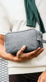 Neceser rectangular color gris oscuro, con doble cierre superior, compartimentos individuales, bolsillo frontal con cierre y correa de mano.