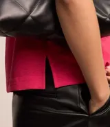 Blusa blanca de poliéster con cuello redondo, mangas cortas, cierre trasero en forma de gota, pequeñas aberturas laterales y acabados en pespuntes en las mangas y el cuello.