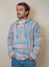 Buzo con capucha de tejido grueso a rayas horizontales en tonos pastel: celeste, rosa y gris. Tiene bolsillo tipo canguro y cordones ajustables en el cuello.